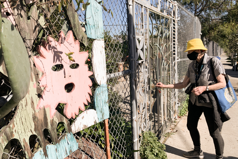 A woman opens a gate to a garden.